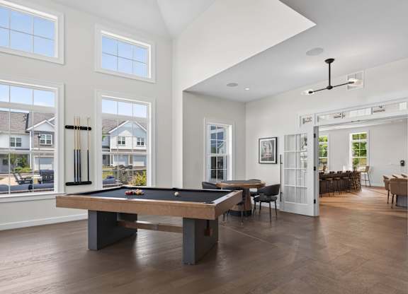 Pool table centered in a bright game room with tall windows and lounge seating.