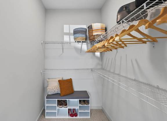 Large closet with wraparound wire shelving, hanging rods, and a storage bench.