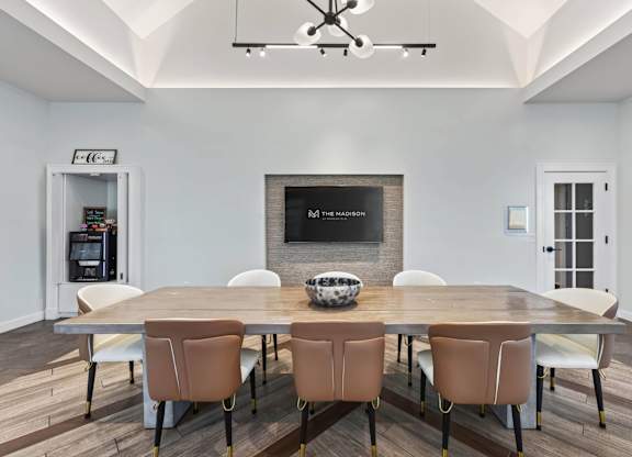 Clubhouse dining table with eight chairs beneath a high ceiling and modern chandelier.