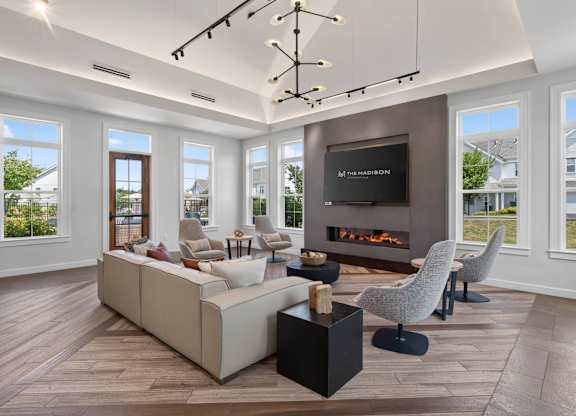 Clubhouse seating area with a sectional sofa, armchairs, fireplace, and tall windows.