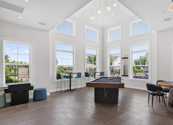 Game room with a pool table, lounge chairs, tall windows, and pendant lighting.