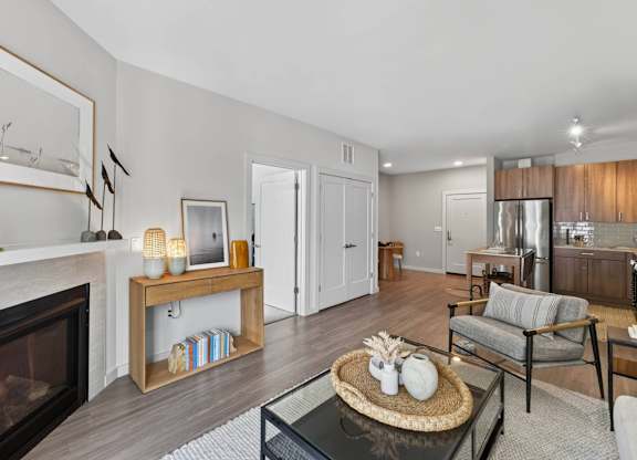 Apartment living room with a gas fireplace, console table, armchair, and open kitchen beyond.