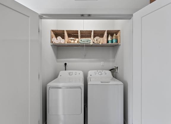 Laundry closet with a full-size washer and dryer beneath open storage cubbies.