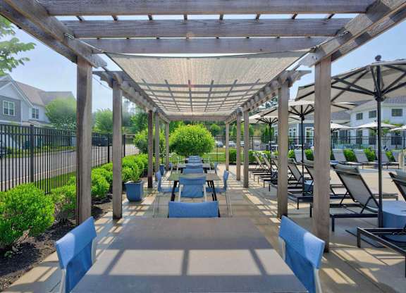 Poolside pergola with cushioned benches, tables, and lounge chairs beside the pool.
