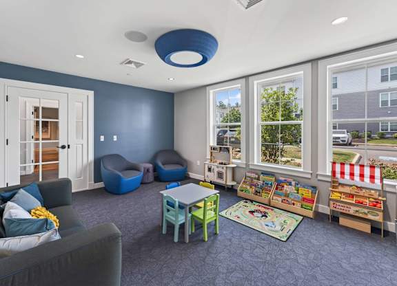 Indoor playroom with a sofa, small tables, book displays, and colorful toys.
