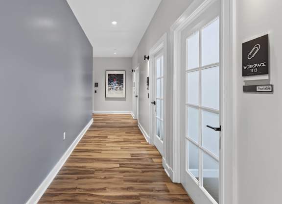Hallway lined with glass-doored work-from-home rooms and wood-style flooring.