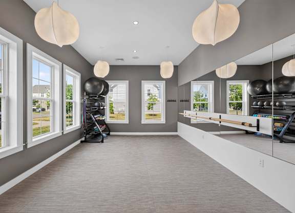 Fitness room with mirrored walls, exercise balls, mats, and large windows.