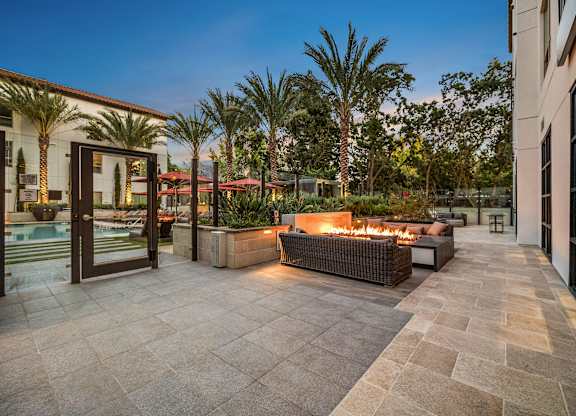 Fire pit lounge with woven seating, glowing flames, and palm-lined views creating a resort-style retreat