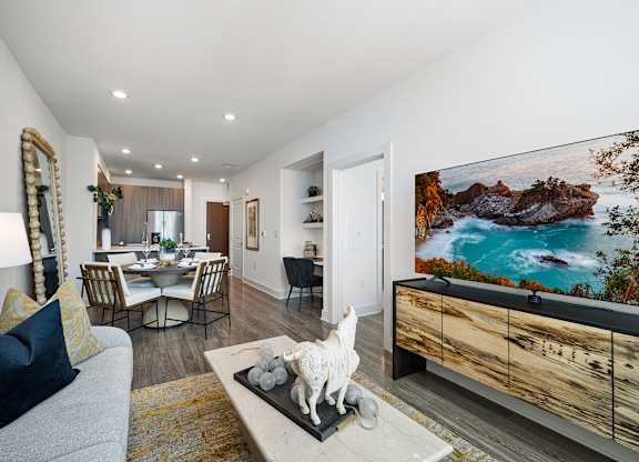 Bright living room with contemporary furnishings, wall-mounted TV, and open dining layout