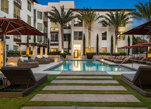 Evening pool deck with illuminated palm trees, cushioned loungers, and a tranquil resort-style atmosphere