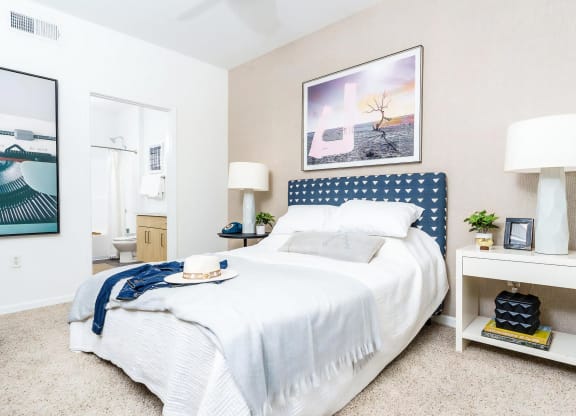Dog-Friendly Apartments In Rancho Cucamonga, CA - Villas At The Gardens - Bedroom With Plush Carpeting, Large Bed, Nightstands With Lamps, And Attached Bathroom.