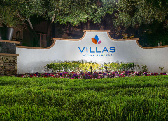 Villas at the Gardens Illuminated Entry Sign with Lush Lawn and Colorful Flowers