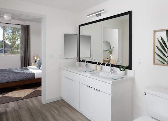 Bathroom with a wide double vanity, two framed mirrors, white cabinetry, and a bedroom doorway.