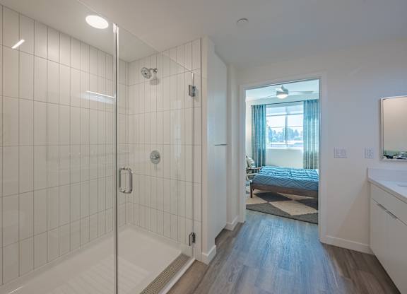 Glass-enclosed shower beside a vanity with a clear view into the adjoining bedroom.