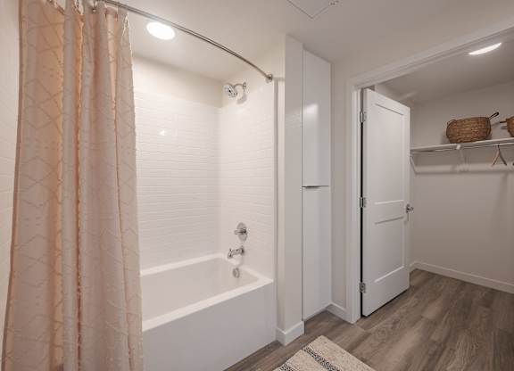 Bathroom with a tub and shower beside an open walk-in closet with built-in shelving.