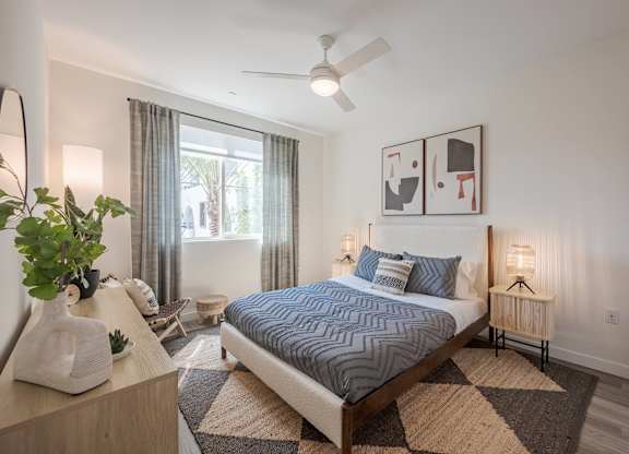 Bedroom with a large window, ceiling fan, wood bed frame, dresser, and abstract wall art.