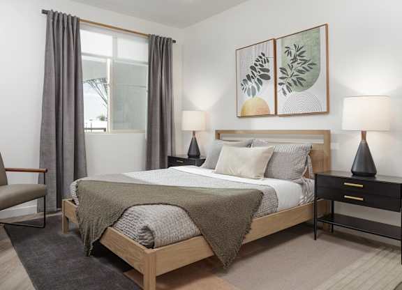 Bedroom with a large window, upholstered bed, bedside tables, chair, and wood-style flooring.