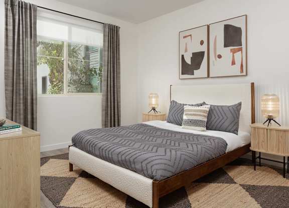 Bedroom with a large window, wood bed frame, dresser, bedside tables, and neutral decor.