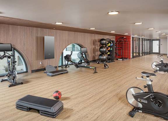 Upper-level fitness studio with stationary bikes, treadmills, strength equipment, and wood-style flooring.