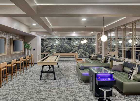 Game lounge with a ping-pong table, counter seating, arcade games, sofas, and televisions.