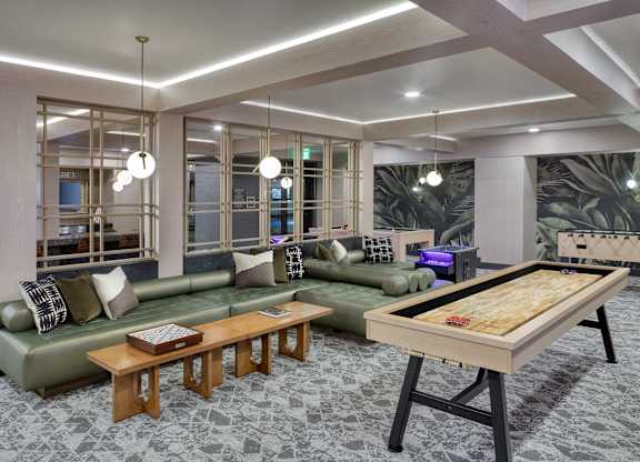 Game lounge with shuffleboard, a sectional sofa, arcade games, televisions, and counter seating.