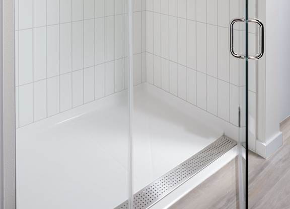 Glass-enclosed walk-in shower with white tile walls, built-in controls, and a metal handle.