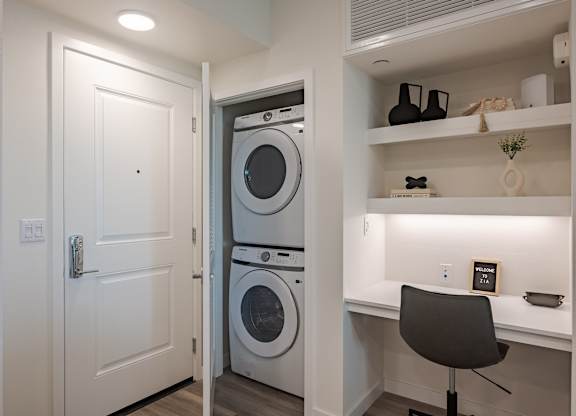 Apartment entry with a stacked washer and dryer beside a built-in desk and open shelving.