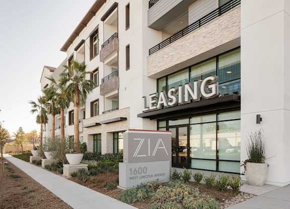 Zia leasing entrance with building signage, landscaped planters, balconies, and a sidewalk.