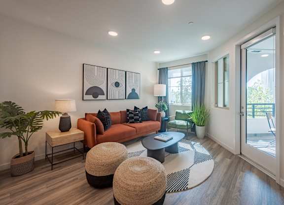 Living room with an orange sofa, round coffee tables, large windows, and a balcony door.