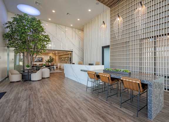 Zia lobby with curved sofas, round tables, a long worktable, greenery, and high ceilings.