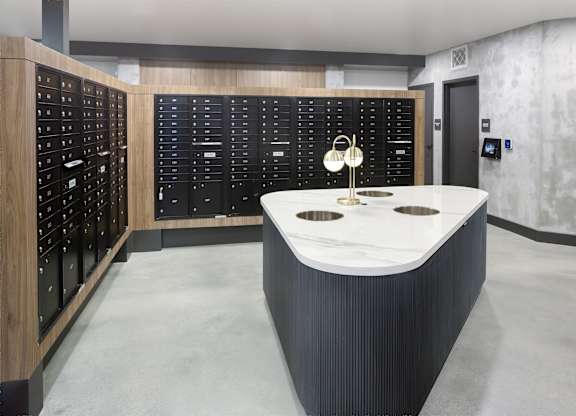 Mail room with rows of parcel lockers, mailboxes, a central counter, and pendant lights.