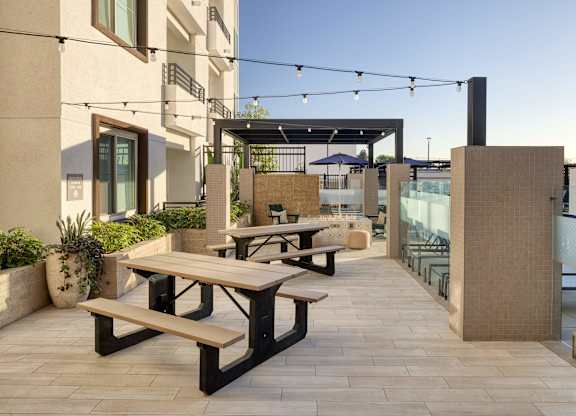 Outdoor dining courtyard with picnic tables, string lights, planters, and a shaded pergola.