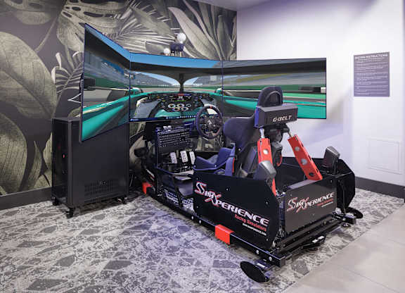 Racing car simulator with a driver's seat, steering controls, and three curved display screens.