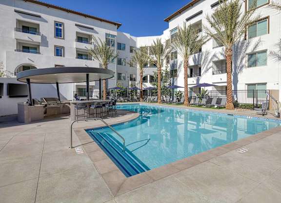 Resort-style pool with palm trees, lounge seating, apartment buildings, and the circular Round Bar.