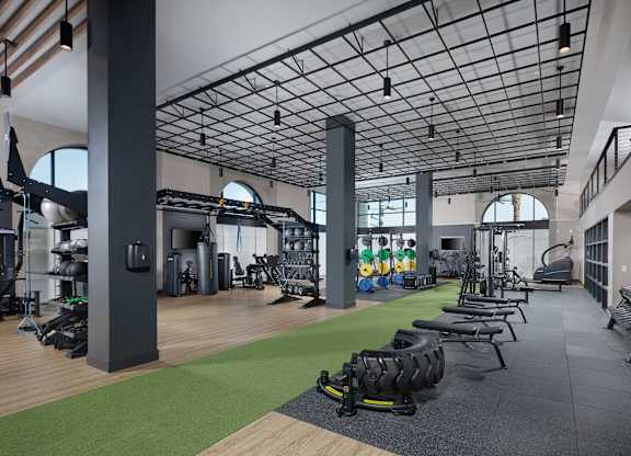 Two-story fitness center with strength equipment, indoor turf, free weights, and large arched windows.