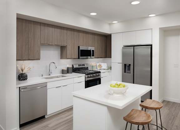 Kitchen with white and wood cabinetry, quartz island, stainless steel appliances, and counter stools.