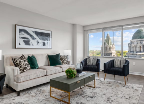 a living room with a beige couch and two black and white chairs and a large window