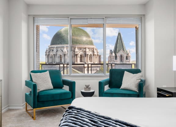a bedroom with a bed and two chairs in front of a window with a view of a