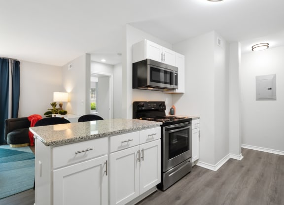 a kitchen with white cabinetry and a counter top with a stove and a microwave