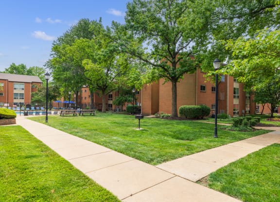 a grassy area with trees and a walkway in front of a brick building