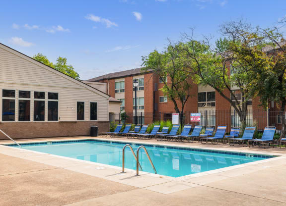 a swimming pool with blue chaise lounge chairs and a brick building in the background