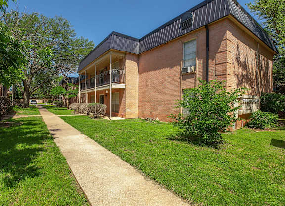 a sidewalk in front of a brick building with grass and trees