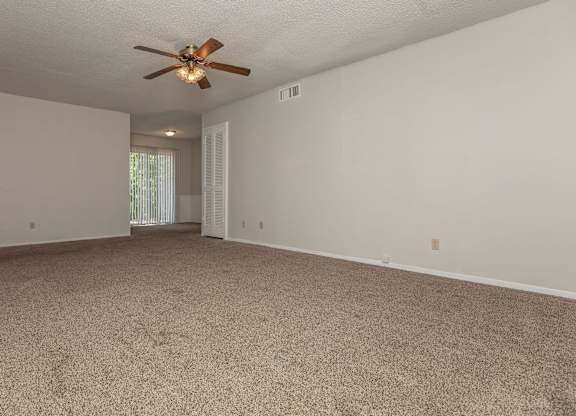 a spacious living room with carpet and a ceiling fan