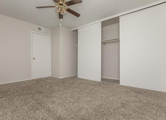 an empty living room with a ceiling fan and closet
