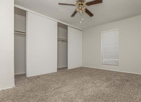 an empty living room with a ceiling fan and a closet
