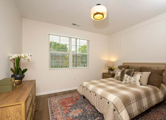 A bedroom with a bed, nightstand, and window with blinds.