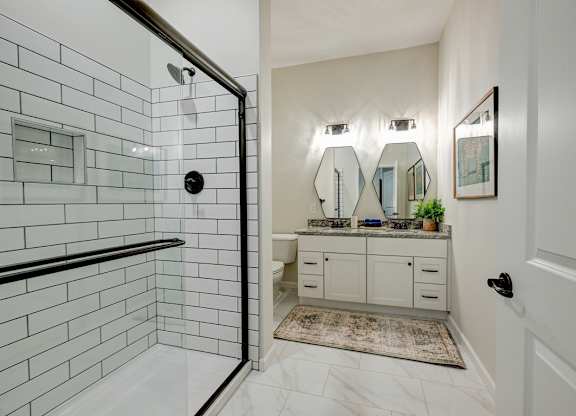 A bathroom with a white tiled shower and a vanity with a mirror above it.