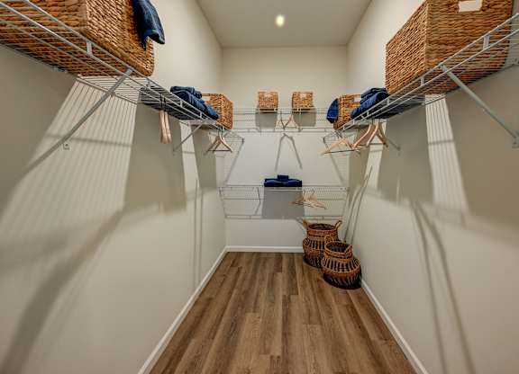 A walk-in closet with white walls and wooden floors.