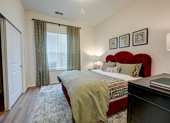 A bedroom with a red headboard and a window with curtains.