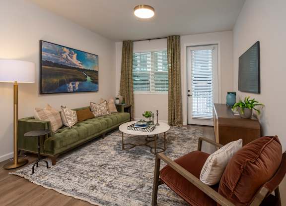 A living room with a green couch, a painting on the wall, and a lamp on a stand.